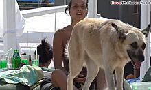छोटे स्तन वाली एक शौकिया लड़की समुद्र तट पर एक कुत्ते के साथ खेल रही है।